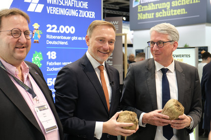 Christian Lindner mit Zuckerrübe in der Hand zwischen zwei Männern. 